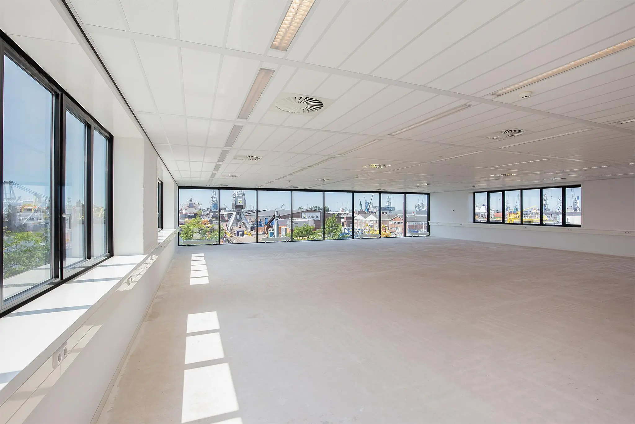 Lichte, leegstaande kantoorruimte met grote ramen en uitzicht op de Waalhaven in Rotterdam.